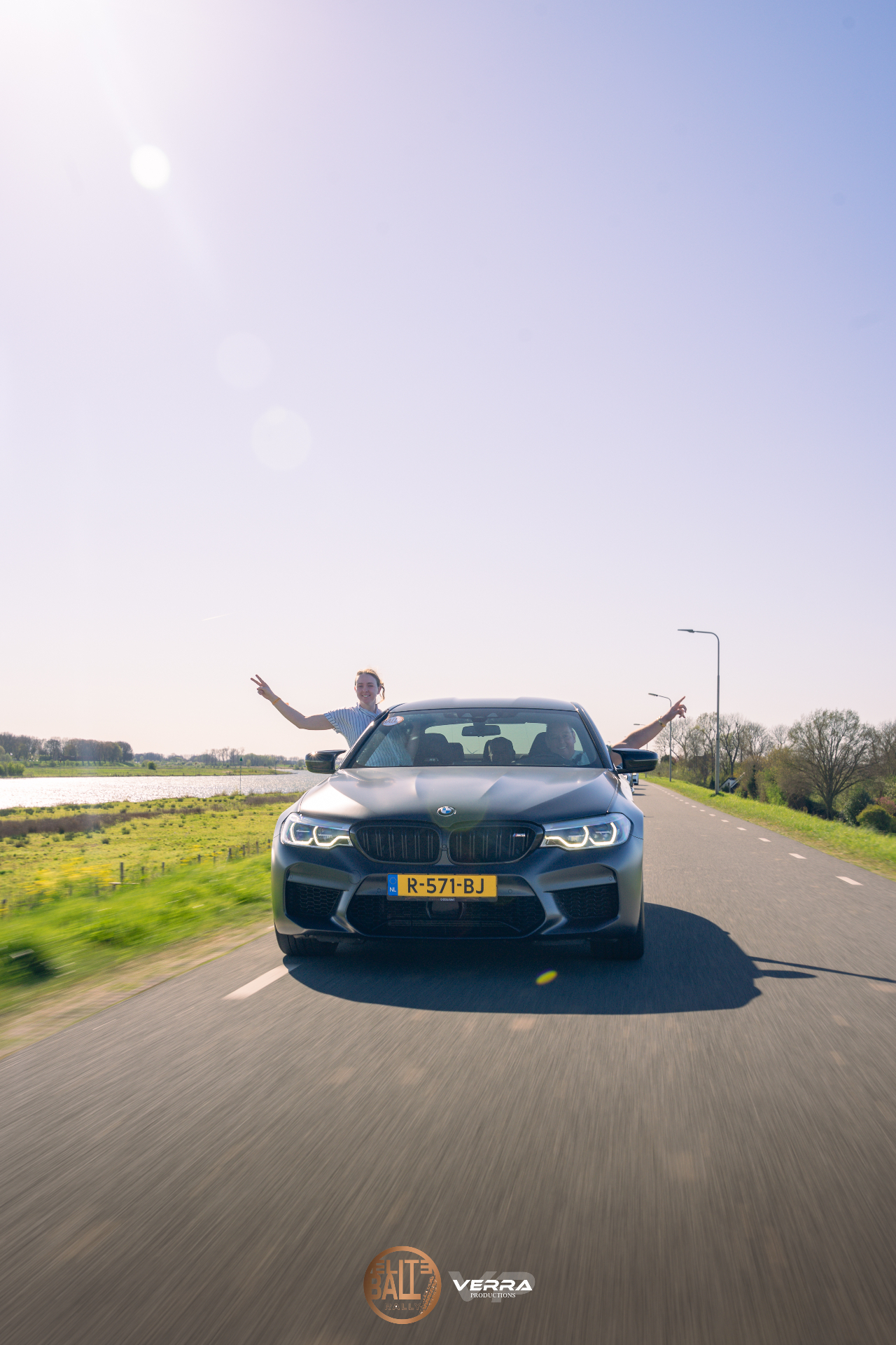 Deelnemers juichen uit het raam van een BMW M5 tijdens Eliteball Rally