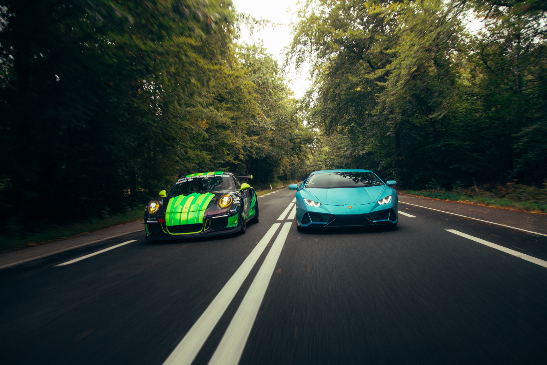 Porsche 911 GT3 RS en blauwe Lamborghini Huracán EVO rijden naast elkaar door bosrijke laan